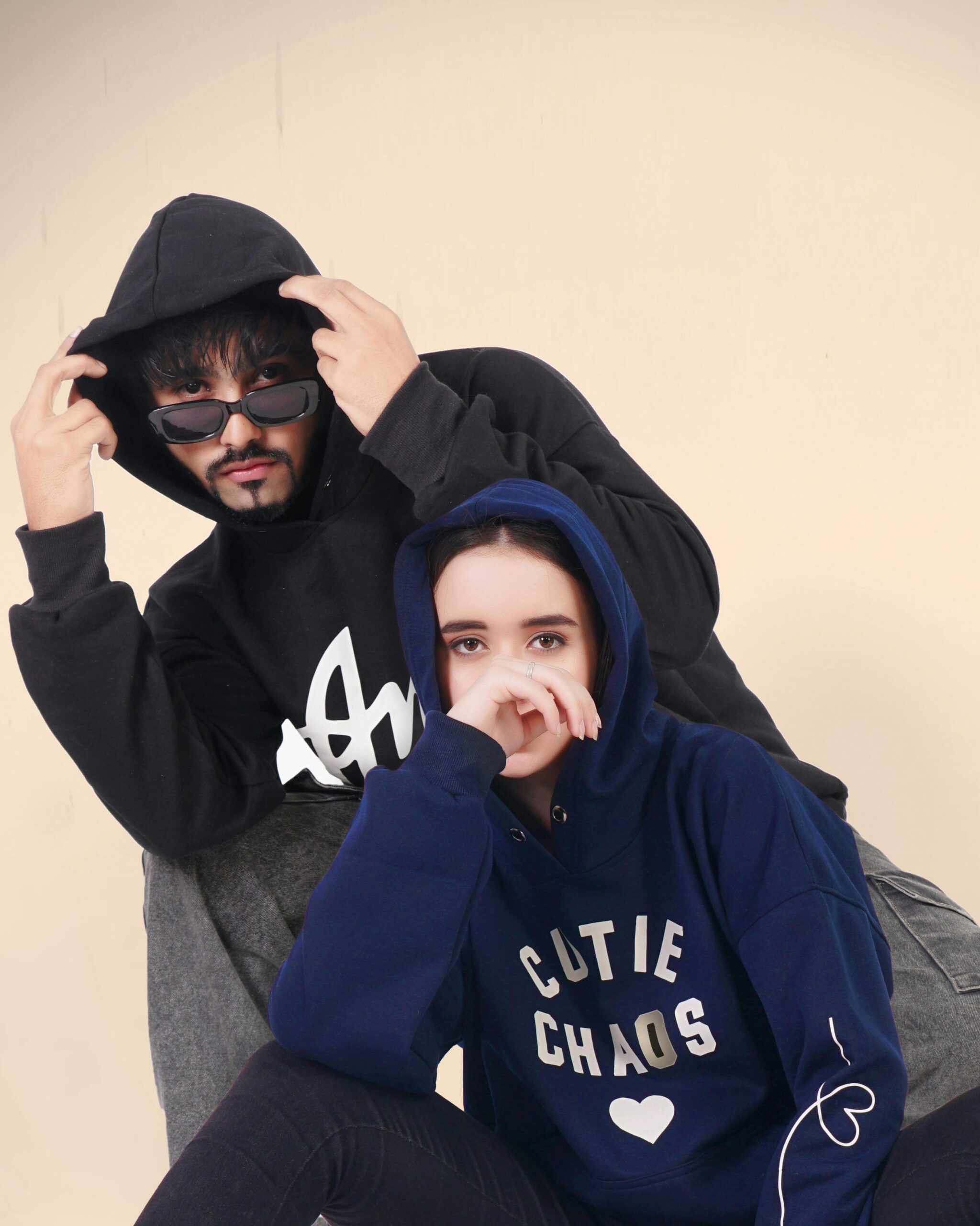 Stylish young man and woman posing in hoodies during a studio fashion shoot.