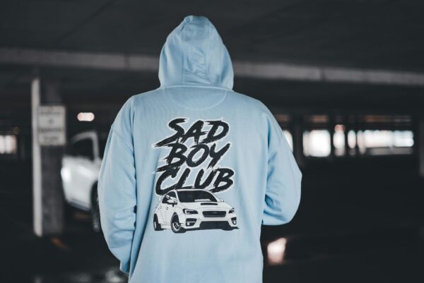 Person in Blue Hoodie with Sad Boy Club Script in Garage